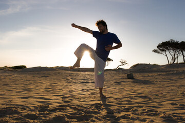 contraluz de hombre practicando artes marciales al atardecer en la playa