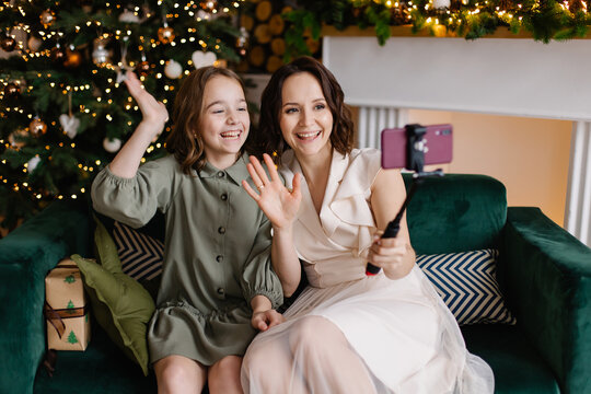 Mother and daughter celebrate Christmas online. Family video call for the new year. Stylish modern interior of a cozy living room. Decorated house for christmas. Selfie Remote communication 