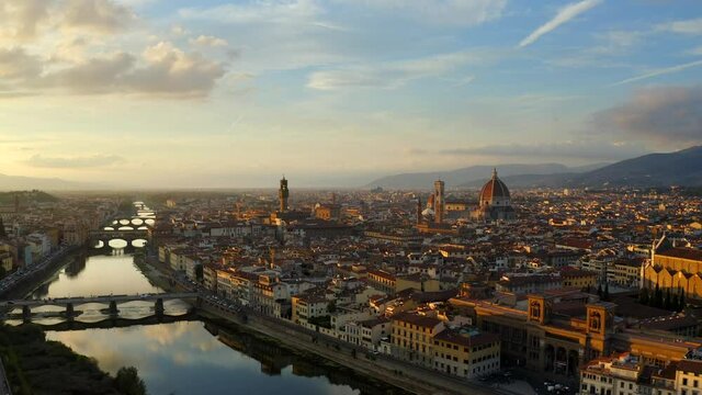 Florence, Tuscany, Italy, October 2021. Drone gradually ascends while pulling back from the Arno river facing west towards the Cathedral of Santa Maria del Fiore and Palazzo Vecchio at sunset.