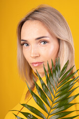 Naklejka premium Beauty portrait of a young, beautiful blonde woman with good skin in yellow clothes holding a green leaf on a yellow background