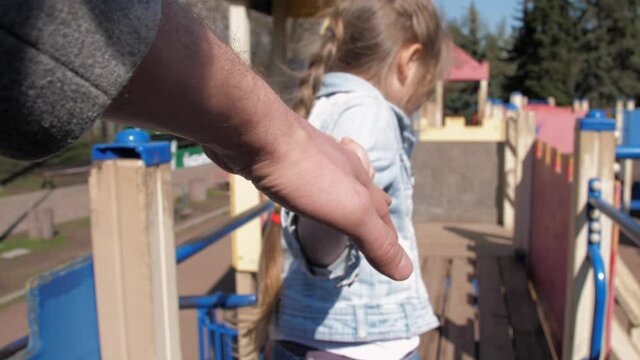 Blonde young schoolgirl holds stepfather hand and walks down brown wooden attraction stairs closeup slow motion. Concept relationship