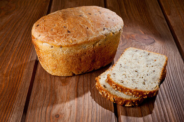 A loaf of delicious white bread made from natural products, on hops with flax saturation, without baker's yeast, on a wooden table surface.