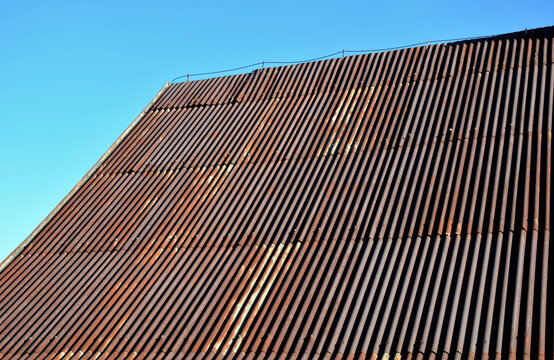 corrugated iron roof with a lightning conductor on top. the sheet is the whole rust and forms a texture similar to Manchester fabric. roof before renovation, blue sky