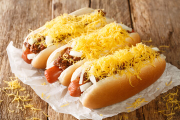 American chili hot dog with beef sausage, cheddar cheese and onions close-up on an old wooden...
