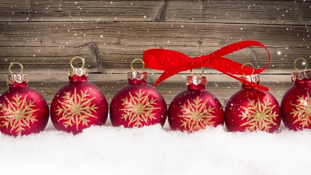 Still life with red ball row on snow covered surface. Wooden desk in the background. Falling snow effect. Christmas, holiday and winter concept. High quality 4k video.