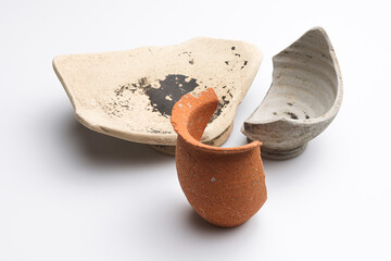 Archeologia: frammenti di vasetti e ciotole di epoca romana di vari materiali e colori isolate su fondo bianco 