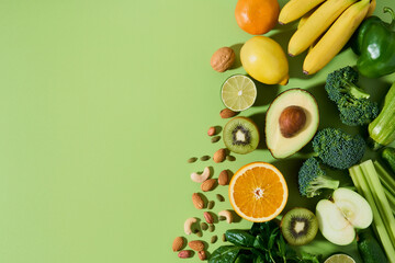 Set of healthy vegetables, fruits and nuts on green background, copy space. Proper balanced products. Avocado broccoli lime kiwi almond celery, lemon and orange, banana and cucumber, cabbage, apple