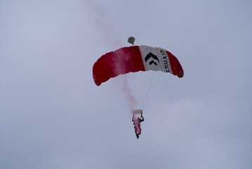 Parachutist with red smoke at Axalp Canton Bern air show of Swiss Air Force on a cloudy grey autumn day. Photo taken October 19th, 2021, Brienz, Switzerland.