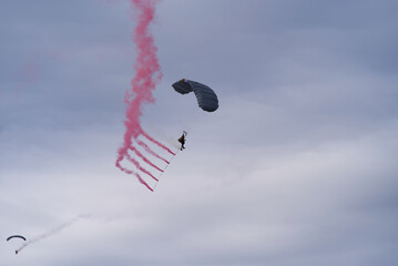 Parachutist with red smoke at Axalp Canton Bern air show of Swiss Air Force on a cloudy grey autumn day. Photo taken October 19th, 2021, Brienz, Switzerland.