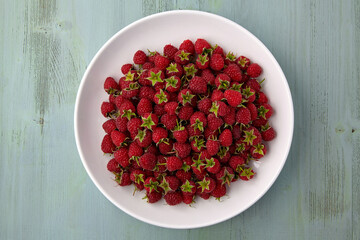 Ripe raspberries with cuttings on a white plate on a blue wooden background