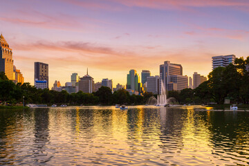 Nature lake in public park at city center with business buildings and sunset sky background, Bangkok