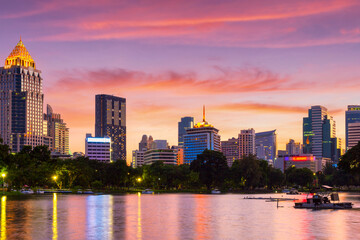 Nature lake in public park at city center with business buildings and sunset sky background, Bangkok