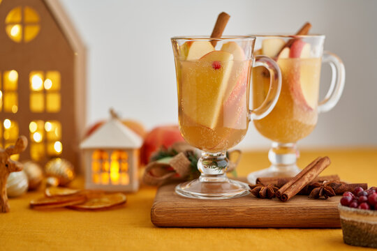 Two glasses of hot christmas winter apple gluhwein. Alcohol white mulled wine with cinnamon, cranberry. Apple cider. Selective focus, blurred christmas garland decor background, horizontal