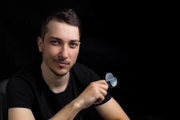 Young handsome man and a magnifying glass on black background in low key. Search symbol....