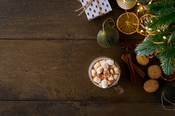 Hot cocoa with marshmallows and grated chocolate on wooden background with christmas decorations, toys and baubles. Festive cozy atmosphere. Top view, copy space
