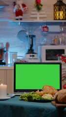 Fototapeta na wymiar Man and woman watching green screen on laptop enjoying festive dinner at christmas celebration. Couple looking at chroma key with mockup template and isolated background, celebrating holiday