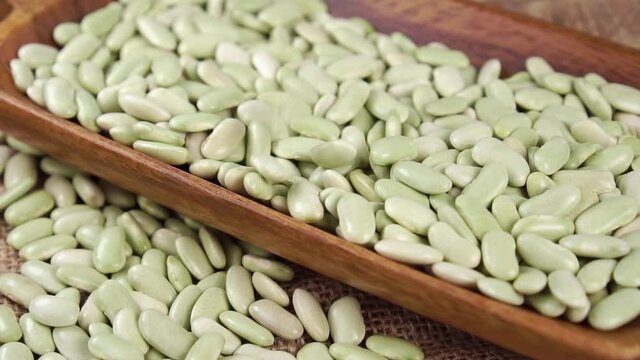 Dry green Verdina beans falling into wooden ware close up. Uncooked legumes from Asturias and Galicia, Spain. Traditional Spanish cuisine. Healthy raw organic food. Slow motion