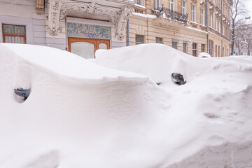 There are cars on the streets of the city. They are covered with a lot of snow. Winter disaster.