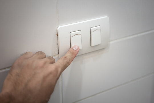 Action of a people is pressing on electric lighting switch to turn-off the light. Energy saving concept and interior object photo. Close-up and selective focus at the people's index finger.