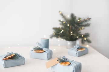 Christmas gift in eco friendly reusable fabric package. Decorated dried orange fruits, fir branches, tag on grey background. Japanese style furoshiki. Top view. Place for text