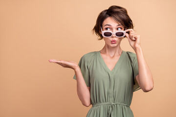 Photo of dreamy shocked happy young woman hand empty space object wear sunglass news isolated on beige color background