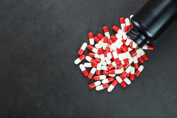 Pills with drugs are scattered from a black jar on a black background.