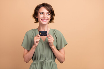 Photo of curious lady showing debit card look empty space wear green dress isolated beige color background