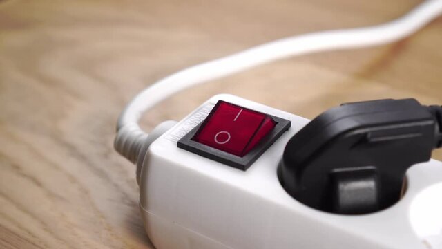 Disconnecting an electrical power strip by pressing a red switch close up. Connected black plug. Electric overload and energy shutdown concept. Pushing button. On a wooden table