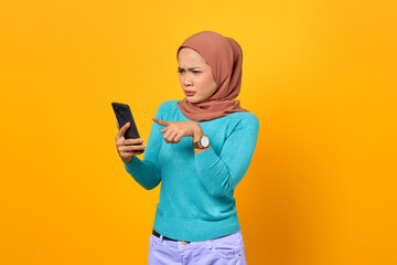 Shocked young Asian woman looking at smartphone screen on yellow background