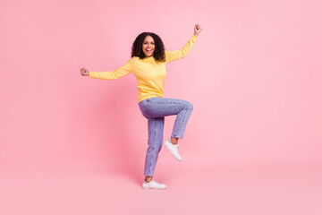 Photo of charming lucky dark skin girl dressed yellow pullover walking rising fists smiling isolated pink color background