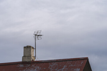 An antenna next to the chimney on a roof of an old shed
