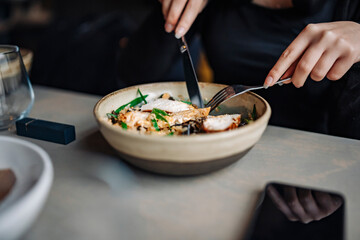 Young woman hand eating donburi with chicken and rice using knife and fork fom bowl