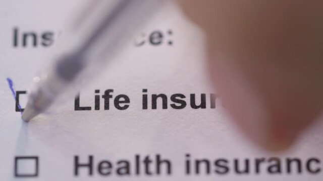 The person ticks off the life insurance item on the form. Close-up. Paperwork.