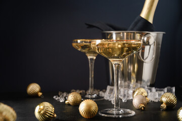 Festive New Year champagne in wine glasses and bottle in bucket decorated Christmas gold baubles on black background. Close up. Holiday greeting card with copy space. © svetlana_cherruty