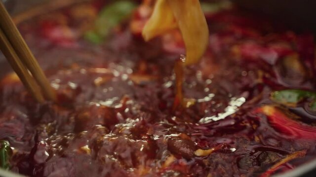 Close-up of Sichuan hot pot Chopsticks holding food in boiling red oil soup