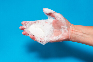 Woman hand holding soap with foam on blue background
