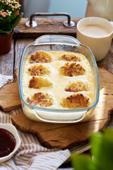 Syrniki baked in a creamy sauce. Wooden and green background. Nuts, rowan twig, side view.