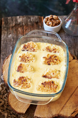 Syrniki baked in a creamy sauce. Wooden and green background. Nuts, rowan twig, side view.