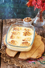 Syrniki baked in a creamy sauce. Wooden and green background. Nuts, rowan twig, side view.