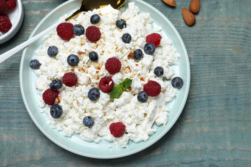 Delicious cottage cheese with fresh berries served for breakfast on light blue wooden table, flat lay
