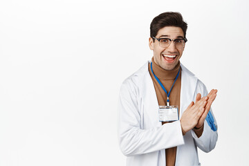 Happy smiling doctor clapping hands, applause and look pleased, standing in medical robe and...