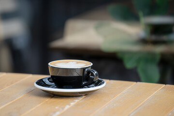 A black cup with cappuccino standing on the table is reflected in the glass wall of the bar counter