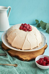 Pavlova cake with raspberries on a white plate and a wooden board. Blue
background, side view.