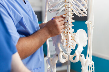 Close up of nurse showing spine bones on human skeleton for diagnosis presentation of senior patient. Medical assistant explaining spinal cord to old man for physical recovery and remedy
