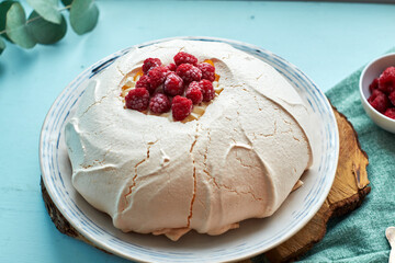 Pavlova cake with raspberries on a white plate and a wooden board. Blue
background, side view.