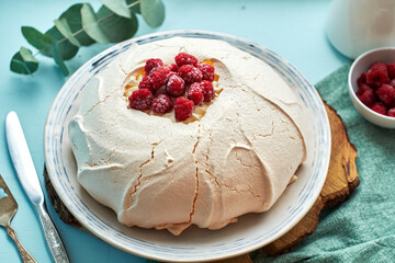 Pavlova cake with raspberries on a white plate and a wooden board. Blue
background, side view.