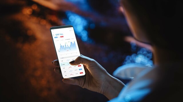 Close-up Shot of Smartphone. Woman is Using Stock Market App to Check Share Prices. Graph is Going Up Making a Great Profit. Beautiful Rainy Night with Neon Refflections.
