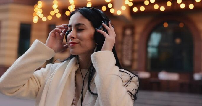 Stylish woman puts on headphones in the city for listening to music