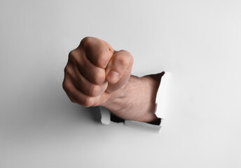 Man breaking through white paper with fist, closeup