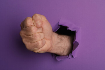Man breaking through purple paper with fist, closeup